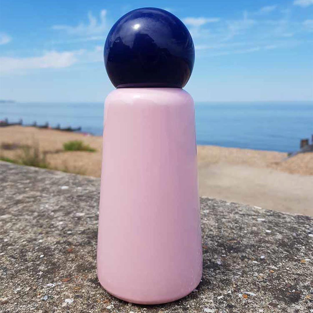 300ml Pink Skittle Water Bottle sat on a sea wall on the British south coast looking out over the beach and sea 